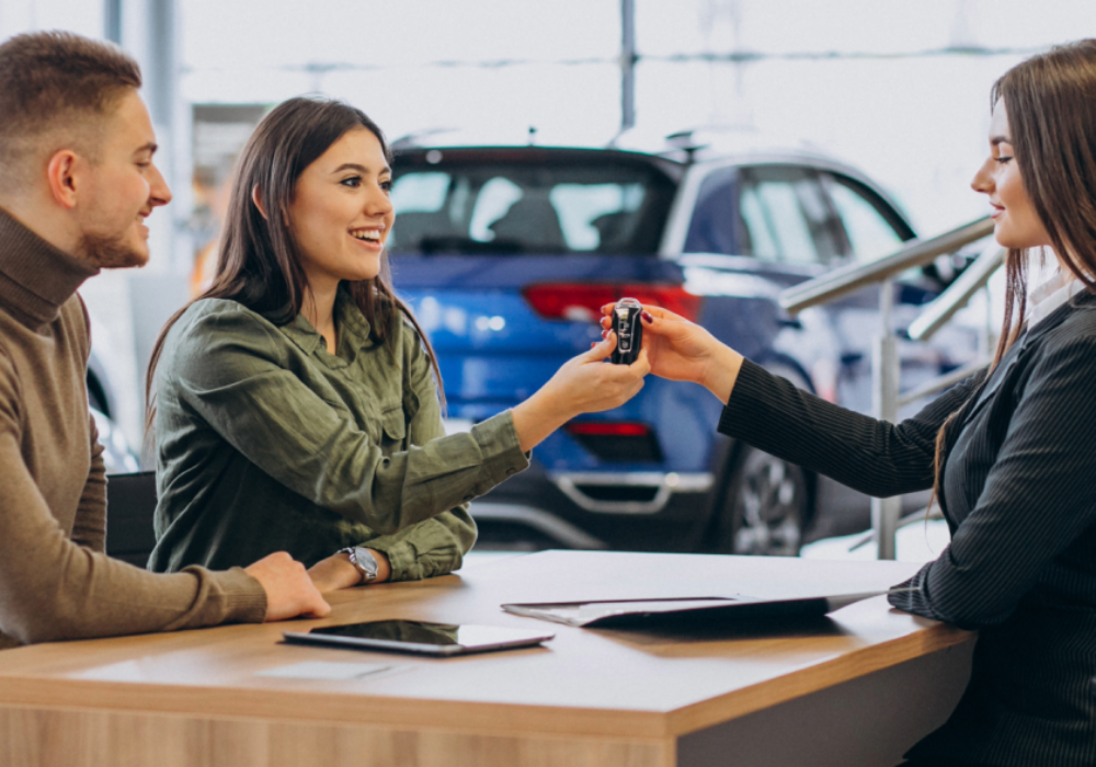 A couple at a car dealership receiving car keys, symbolising the ease of hiring a car for their travels with comprehensive insurance coverage from Islands.